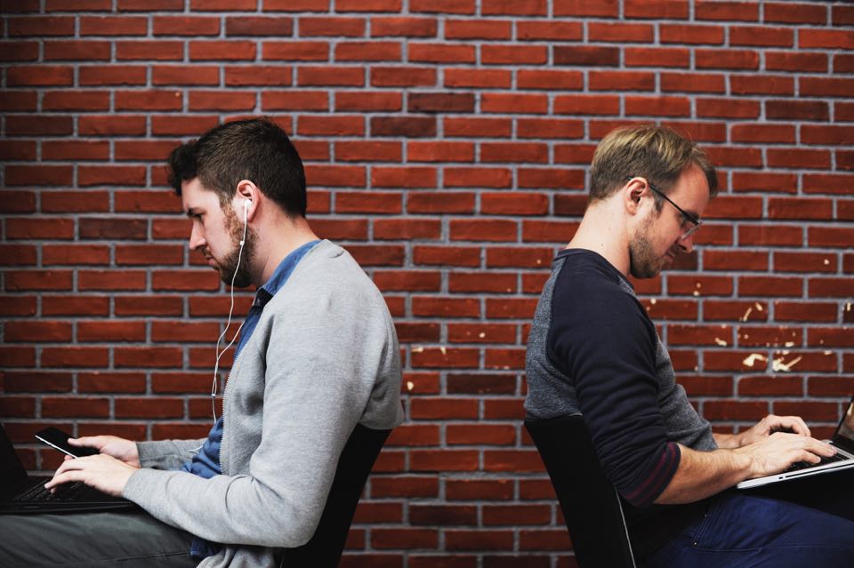 Two men work on computers facing in opposite directions.