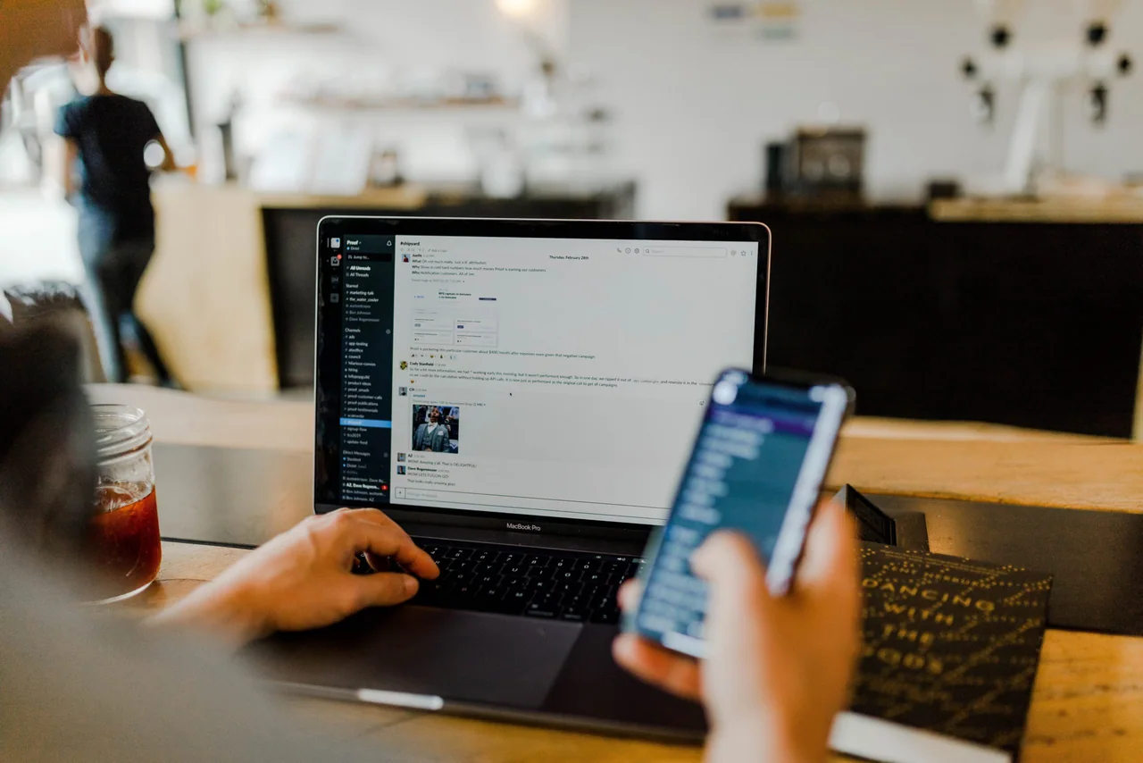 A laptop showing a team messaging dashboard next to a phone, on a cafe table