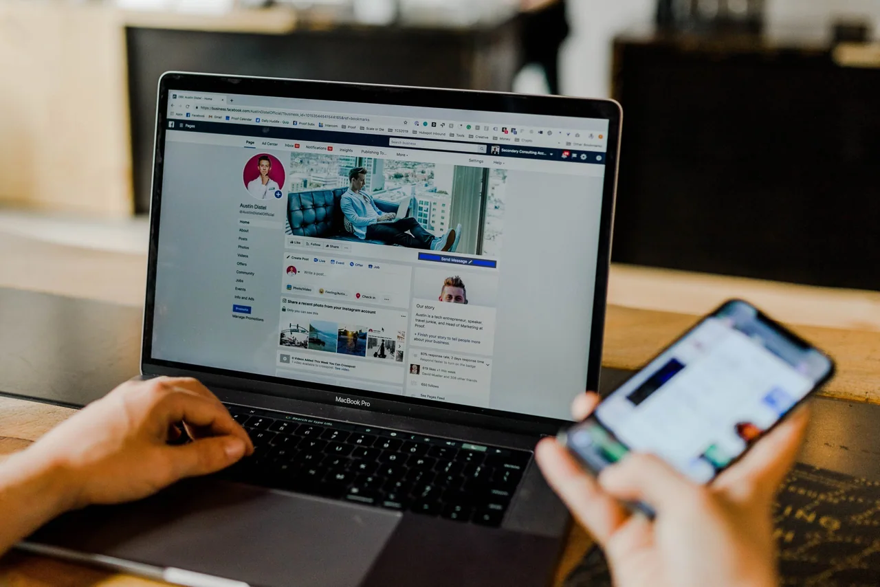 Someone checking a business Facebook page on a laptop while holding a phone