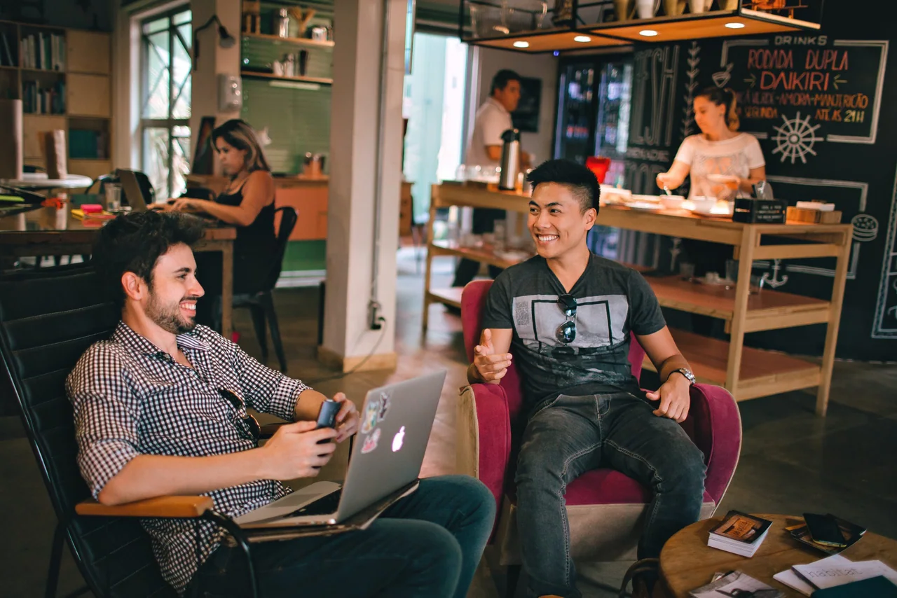 Two colleagues chatting in a casual workspace with a laptop