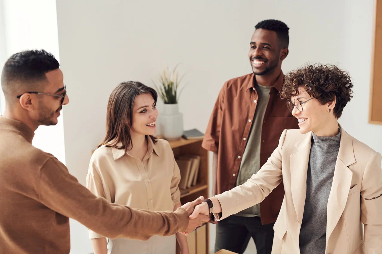 Four colleagues in an office, two of them shaking hands on a deal