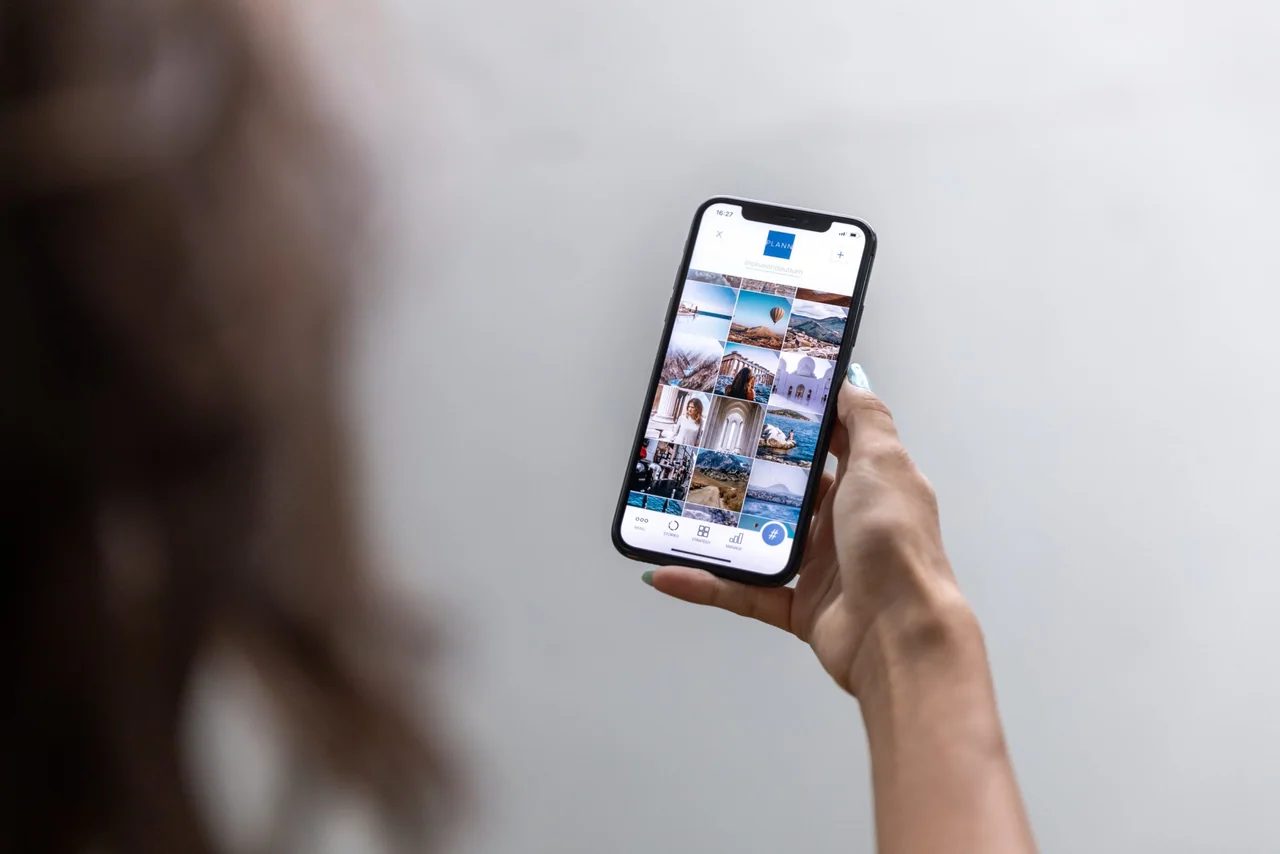 A hand holding a phone one-handed, scrolling a grid of photos in a mobile app