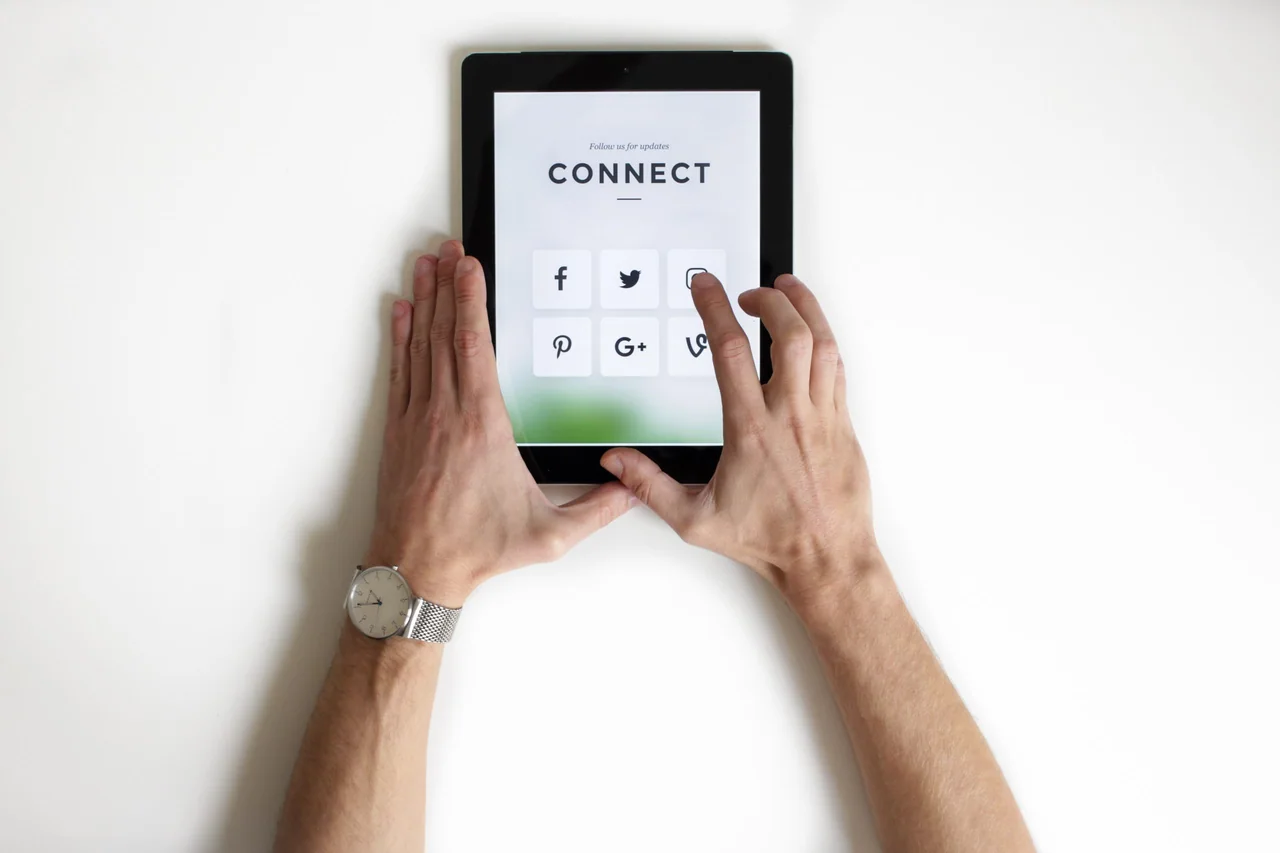 Two hands holding a tablet showing a simple Connect screen with social media icons