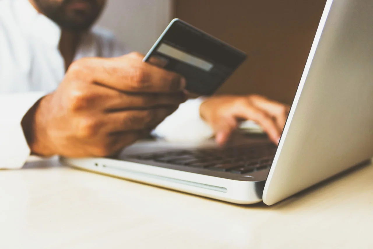 Close-up of a hand holding a credit card beside an open laptop keyboard, making an online card payment