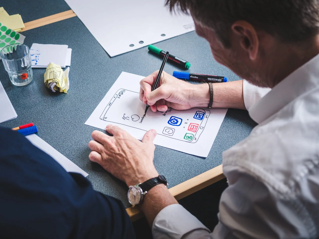 A person drawing a paper prototype of a phone app screen with coloured pens