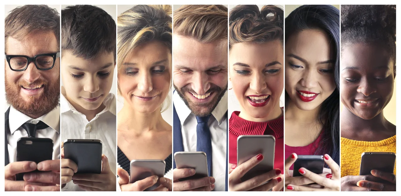 Seven people of different ages smiling as they look down at their phones