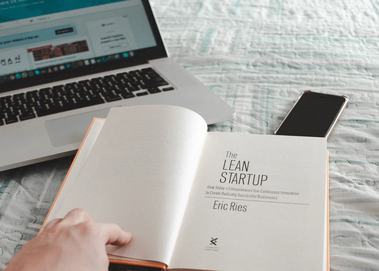 The Lean Startup by Eric Ries, open at its title page, next to a laptop and phone